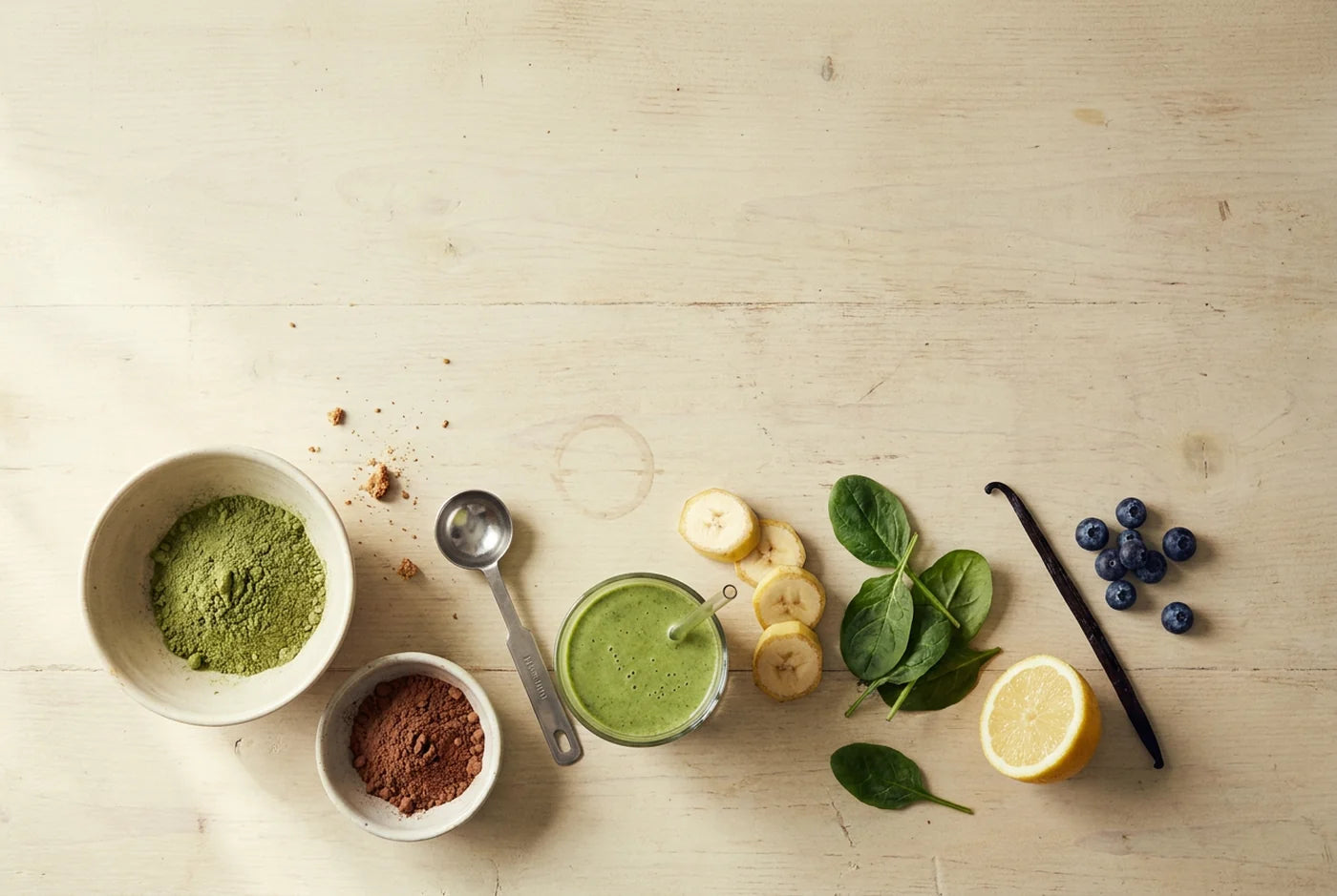 Overhead flat lay of superfood powders, fresh fruit and a green smoothie on a timber bench